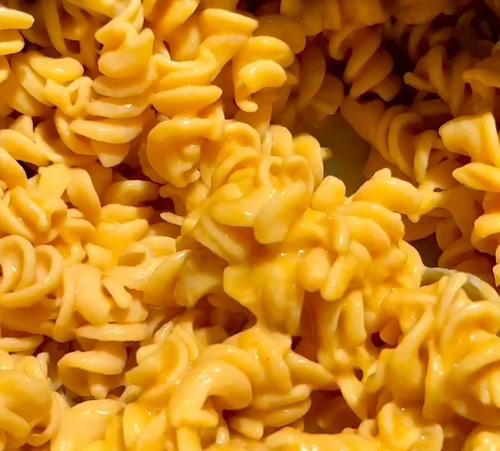 Close-up of creamy, cheesy rotini pasta, showcasing the spirals coated in a rich, orange cheese sauce. The texture looks smooth and the pasta appears well-cooked and appetizing.