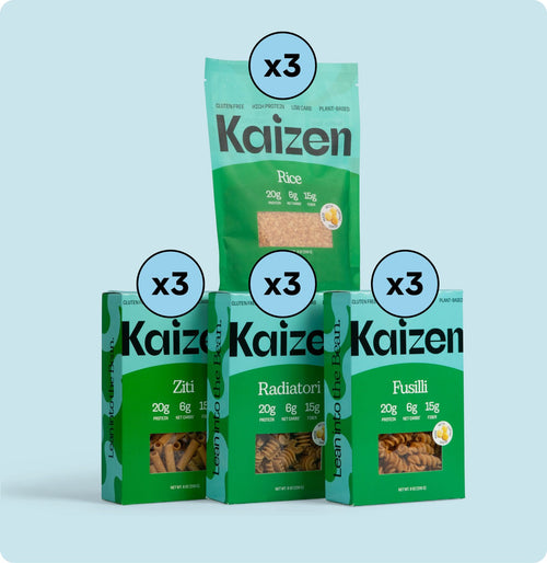 Four green packages of Kaizen brand pasta and rice varieties displayed against a light blue background. The products include rice, ziti, radiatori, and fusilli. Each label highlights 20g protein, 6g fiber, 15g net carbs. Each type is labeled x3.